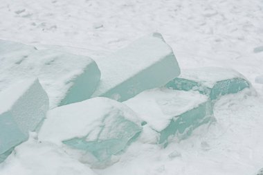 Taze beyaz kar üzerinde dinlenen şeffaf buz bloklarının yer aldığı soyut kış sahnesi, donmuş dokular, serin tonlamalar ve soğuk açık havada minimalist doğal formlar sergiliyor.