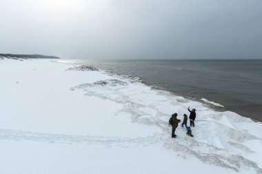 Donmuş dalgalarla buzlu kış deniz manzarası, karlı bir kıyı şeridi boyunca yüzen buzlar ve Litvanya 'nın Palanga kentindeki Baltık Denizi' nde yürüyen insanlar.