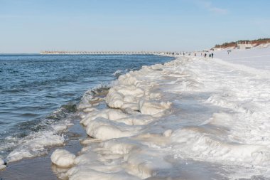 Donmuş dalgalarla buzlu kış deniz manzarası, karlı bir kıyı şeridi boyunca yüzen buzlar ve Litvanya 'nın Palanga kentindeki Baltık Denizi' nde yürüyen insanlar.