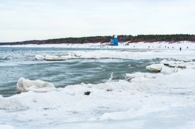 Donmuş dalgalarla buzlu kış deniz manzarası, karlı bir kıyı şeridi boyunca yüzen buzlar ve Litvanya 'nın Palanga kentindeki Baltık Denizi' nde yürüyen insanlar.
