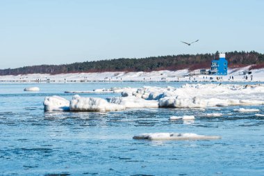 Donmuş dalgalarla buzlu kış deniz manzarası, karlı bir kıyı şeridi boyunca yüzen buzlar ve Litvanya 'nın Palanga kentindeki Baltık Denizi' nde yürüyen insanlar.