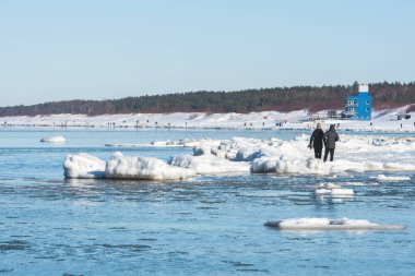 Donmuş dalgalarla buzlu kış deniz manzarası, karlı bir kıyı şeridi boyunca yüzen buzlar ve Litvanya 'nın Palanga kentindeki Baltık Denizi' nde yürüyen insanlar.