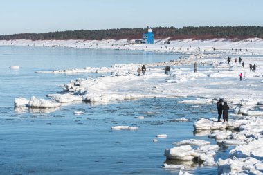 Donmuş dalgalarla buzlu kış deniz manzarası, karlı bir kıyı şeridi boyunca yüzen buzlar ve Litvanya 'nın Palanga kentindeki Baltık Denizi' nde yürüyen insanlar.