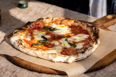 Domates soslu pizza, taze mozzarella peyniri ve ahşap bir tahtanın üzerinde dumanlı fesleğen yaprakları.