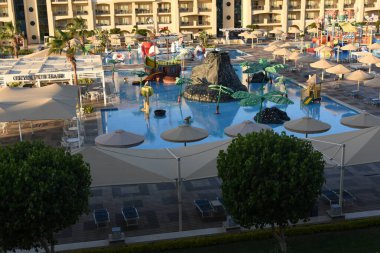 Ağaçlarla ve farklı renkte süslü çalılarla, desenli dekoratif yapraklarla her zaman yeşil yüzme havuzlarının ve doğu tarzında binaların yanında