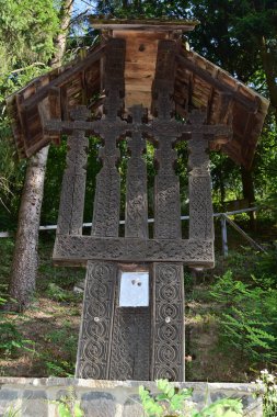 Yolun kenarındaki haç, ortodoks haç ve güneş rozetlerinin baskın olduğu motiflerle tahtadan oyulmuştur. Kötü ruhları uzak tutmak için çatal ve yol kesişimlerinde bulunur.