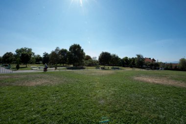 Egzotik ağaçları olan Infinity Sütun Parkı, sütun erişim sokağı, turist bankları ve iyi bakımlı çimenlikleri