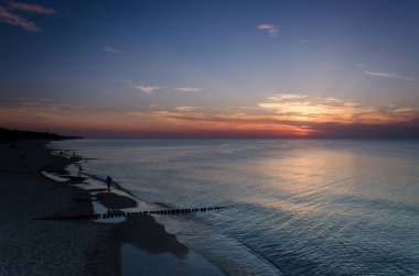 Deniz kıyısında gün batımında insanlar sahilde yürüyorlar. 