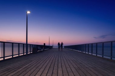 Deniz kıyısındaki PIER Kadınlar sessiz bir günbatımında yürür 