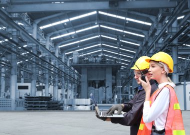 Hard Hats 'daki Erkek ve Kadın Endüstriyel Mühendisler Dizüstü bilgisayar kullanırken Yeni Projeyi Tartışıyor. Ağır Sanayi İmalat Fabrikasında çalışıyorlar..