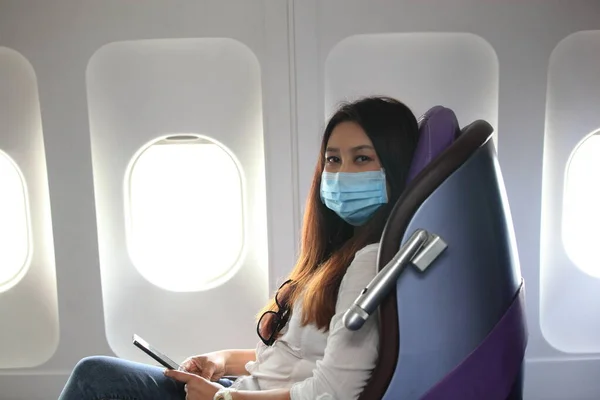 Asian woman tourist on airplane,  medical protective sterile mask on his face traveling. Pandemic covid-19. Safety in public transport.Coronavirus flu virus travel concept