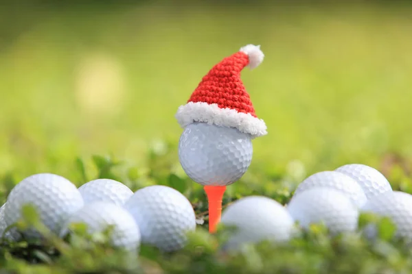ゴルフコースの背景のホリデーシーズンのコンセプトのためのサンタクロースの帽子とティーの上のゴルフボール — ストック写真