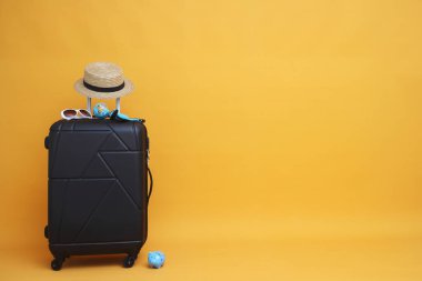 Güneş gözlüklü siyah bavul, pastel sarı arka planda şapka. seyahat konsepti. en küçük biçim