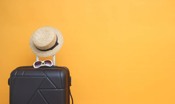 Black suitcase with sun glasses, hat  on pastel yellow   background. travel concept. minimal style