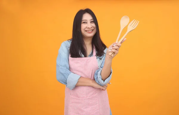 快乐的亚洲女人正在用围裙做饭 因为她们在黄色的背景上做广告 — 图库照片