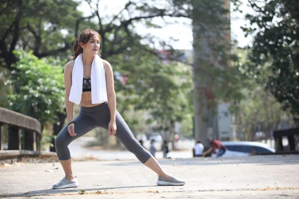 Fitness runner body close up doing warm-up routine before running, stretching arm muscles with standing single, female athlete preparing legs for cardio workout.