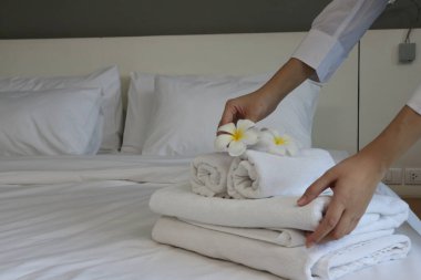 Genç bir otel hizmetçisi temiz havlularla yatağı yapıyor.