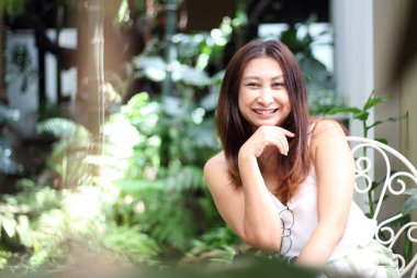  Avluda doğa mobilyalarının keyfini çıkaran bir kadın. Yeşil bahçe terasında sandalyede oturan genç bir kadın, ev hayatı, tatil köyü. 