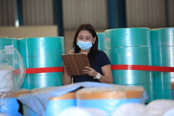 worker woman  with mask on face she are checking stock at  warehouse  ,woman worker with medical mask holding clipboard and checking inventory in the warehouse during coronavirus (covid-19) pandemic