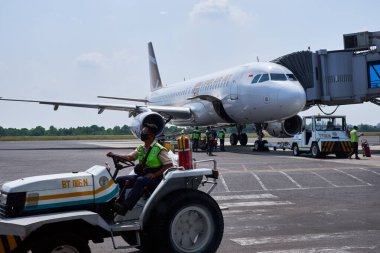 Havaalanı servis aracı park halindeki ticari bir uçağın önünde aprondan geçiyor..
