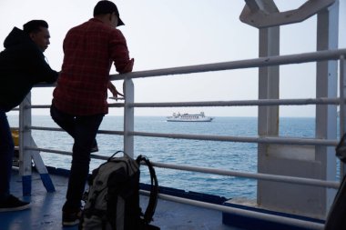 Feribot güvertesinde bekleyen yolcular adalar arası yolculuk sırasında denizi geçen başka bir feribot gemisini izliyorlar..