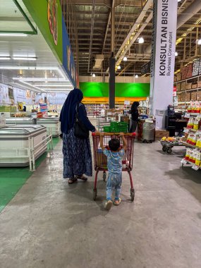 Bir kadın ve çocuk süpermarket koridorunda alışveriş arabalarını iterken perakende mağazasından taze gıda ürünleri alıyorlar..