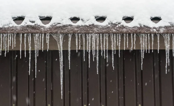 Icicles hang from the roof with snow.