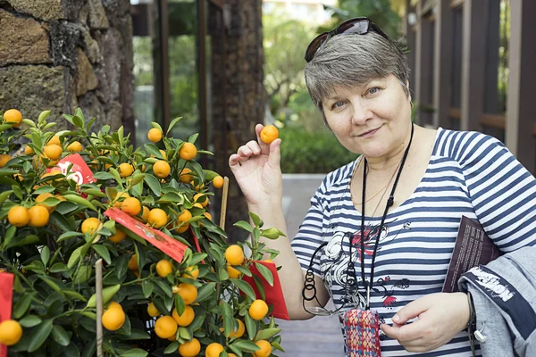 Niedliche Frau hält Mandarine in der Nähe von Mandarinenbusch — Stockfoto