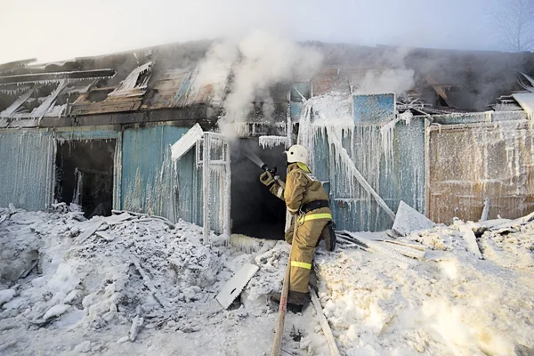 Bombero apaga un fuego en una casa de madera en el invierno . —  Fotos de Stock