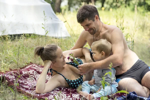 Jonge vader, moeder en zoon 1.3 jaren liggen op het gras in picknick. Man geeft vrouw bloemen. — Stockfoto