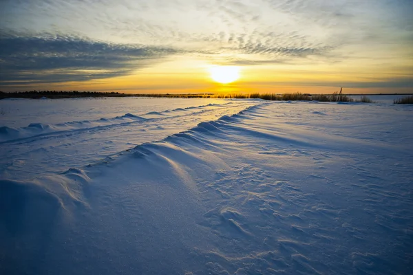 Ljusa solen solnedgång vinter med väg- och fotspår i snön. — Stockfoto