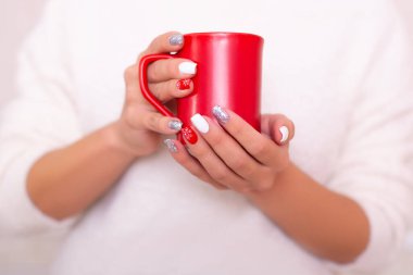Manikür tırnaklı güzel kadın elleri, Noel tasarımı, elinde kırmızı çay bardağı.