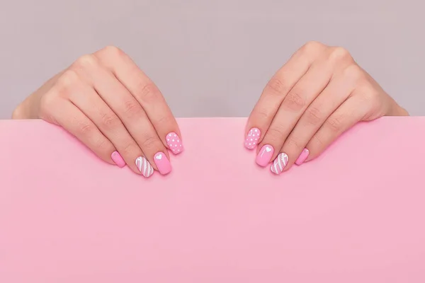 Beautiful female hands with fashion manicure nails, white gel polish, heart design, on pink background with place for text