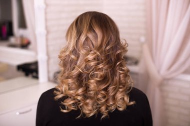 Kıvırcık saçlı, kumral saçlı, kuaförde bir kadın.