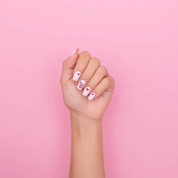 Beautiful female hand with creative manicure nails, hearts and Valentine\'s day design, on pink background