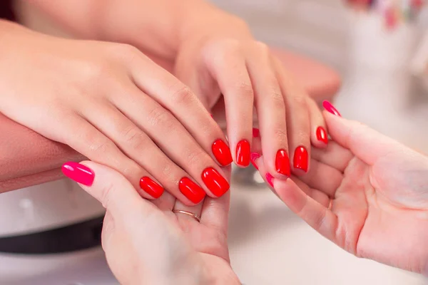 Nail master holding woman hands with red manicure in beauty salon