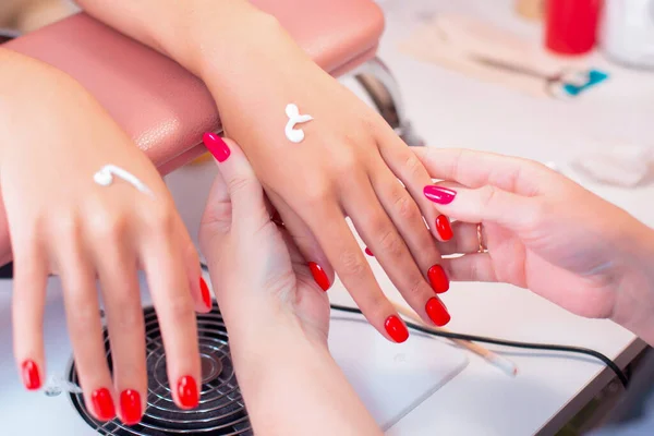Nail master holding woman hands with red manicure in beauty salon and applying cream