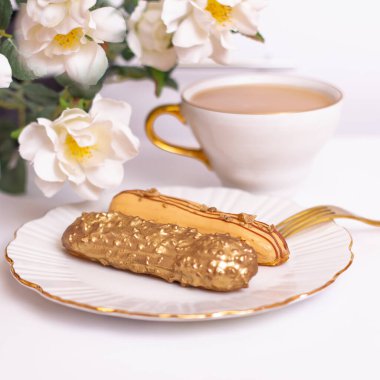 Tabakta altın renkli ekler çatallı ve bir fincan çayla, çiçek buketiyle