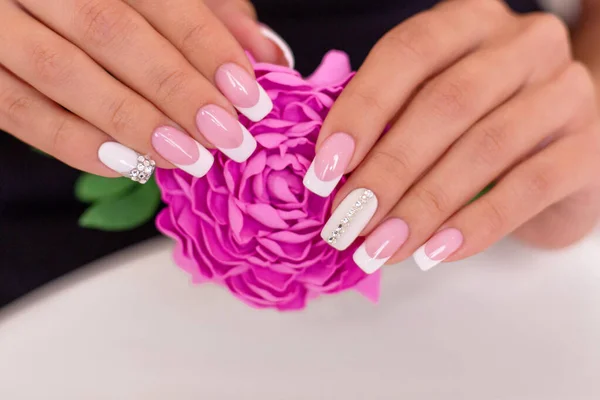 Beautiful female hands with luxury french manicure nails holding pink peony flower