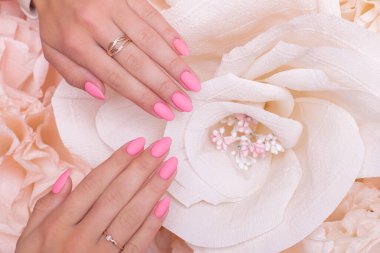 Female hands with wedding manicure nails, pink gel polish, on paper flowers background