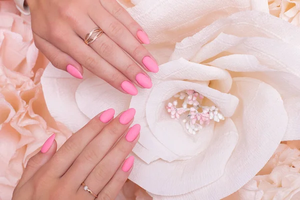 Female hands with wedding manicure nails, pink gel polish, on paper flowers background