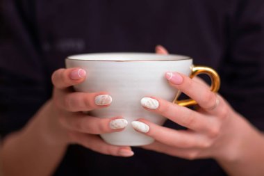 Manikür tırnakları olan, elinde çay tutan bir kadın eli.