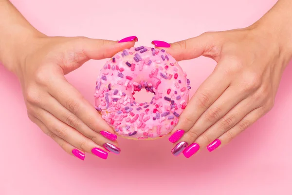 Female hands with pink manicure nails holding sweet strawberry donut