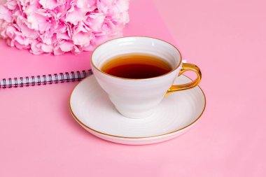Bir fincan çay, defter ve pembe arka planda fotokopi alanı olan ortanca.