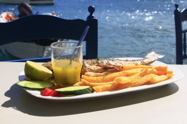 Yunan salatası ve beyaz şaraplı Dorada balığı ve patates kızartması suya yakın bir masada servis ediliyor, Girit Adası, Yunanistan