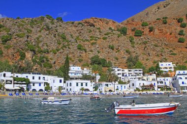 Small fisher boats and sail ships anchored in Loutro with pristine blue water and traditional white buildings, taverns and restaurants, Loutro, Crete, Greece clipart