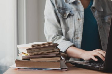 Çalışmak için dizüstü bilgisayar kullanan bir kadın ve kitap yığını ofis masasında..