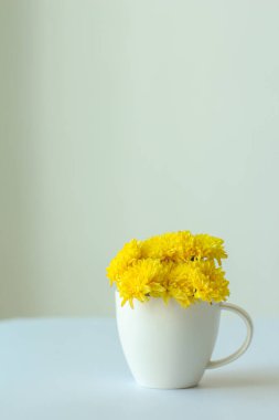 Beyaz masadaki beyaz fincanda sarı çiçek minimal stil.