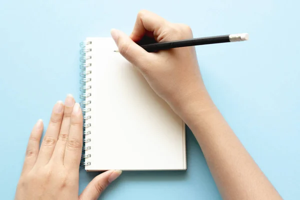 女人的手放在蓝色书桌的空笔记本上写字 平面放置顶部视图 — 图库照片