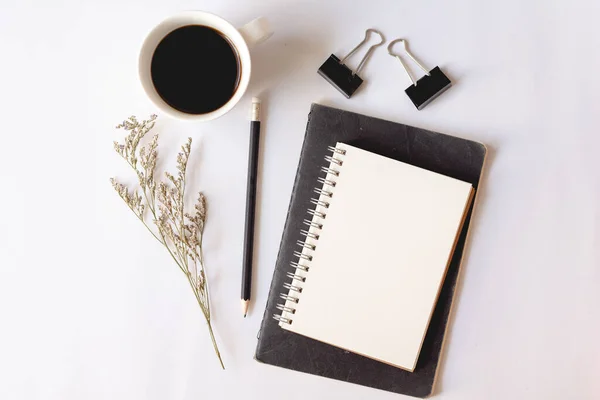 Kağıt defter, kalem, bir fincan kahve ve beyaz arka planda kuru çiçekler. Ofis masaüstü görünümü. En düşük biçim.